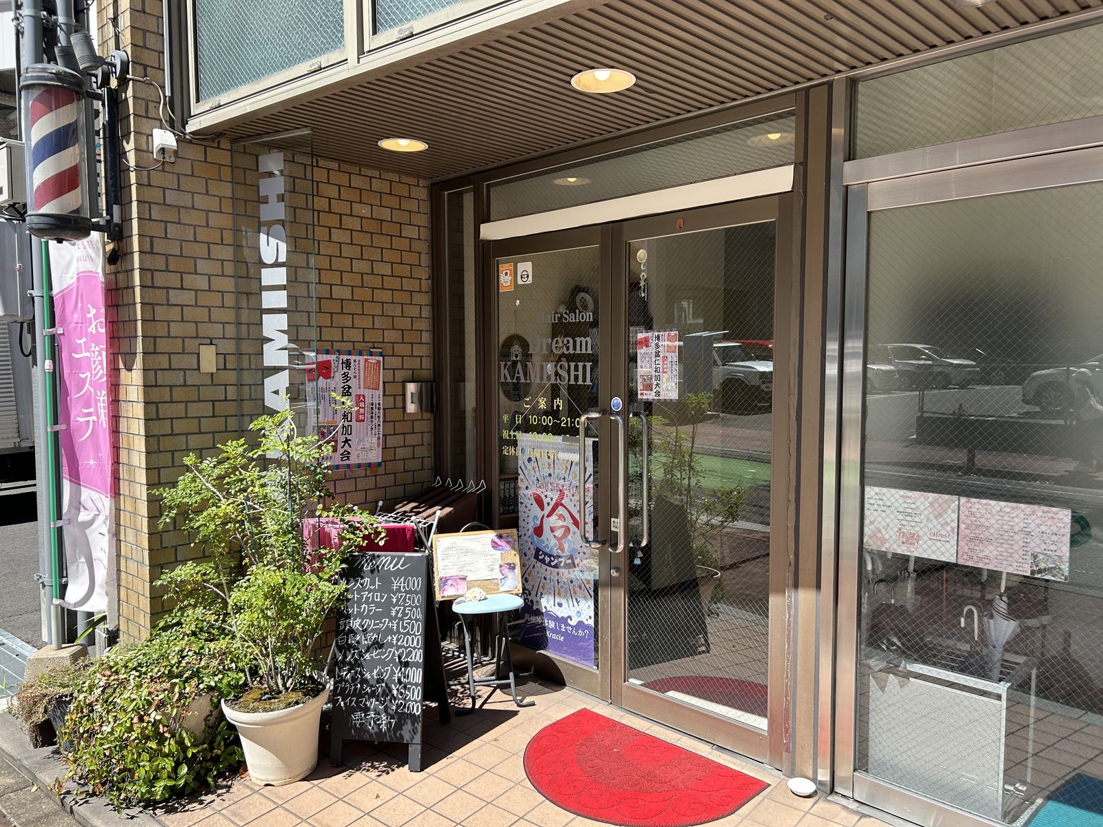 ヘアーサロンDreamKAMIISHI の入り口。ガラス扉に店名と営業時間の案内が出ていて、脇に料金の書かれた黒板が置かれている